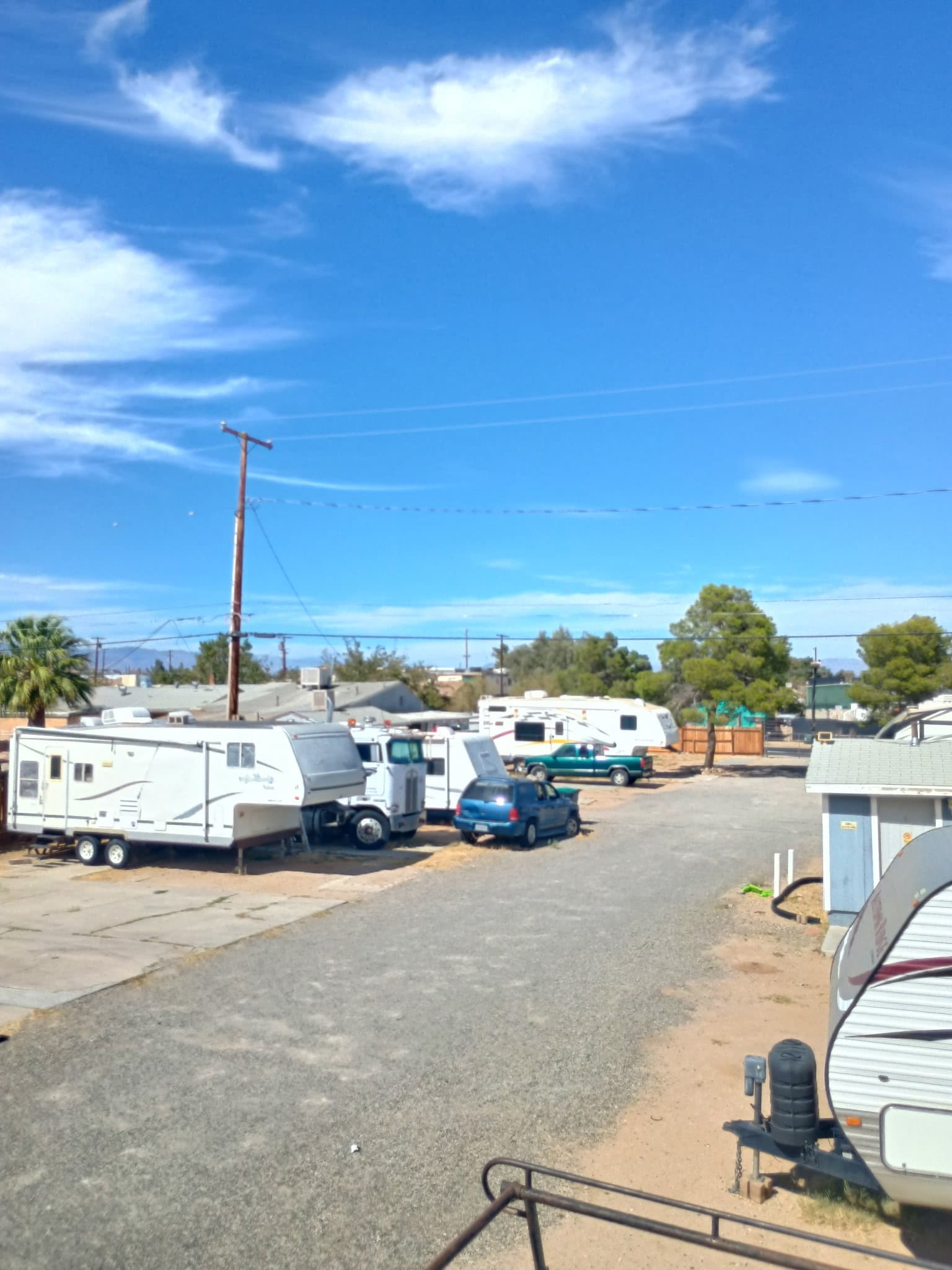 RVs parked along the gravel lane at Village Lane RV Park under a blue desert sky